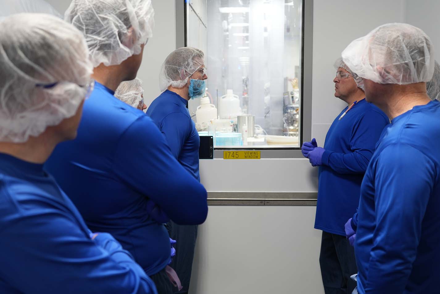 A group of visitors wearing blue PPE and hairnets tours the Zoetis Charles City manufacturing facility.